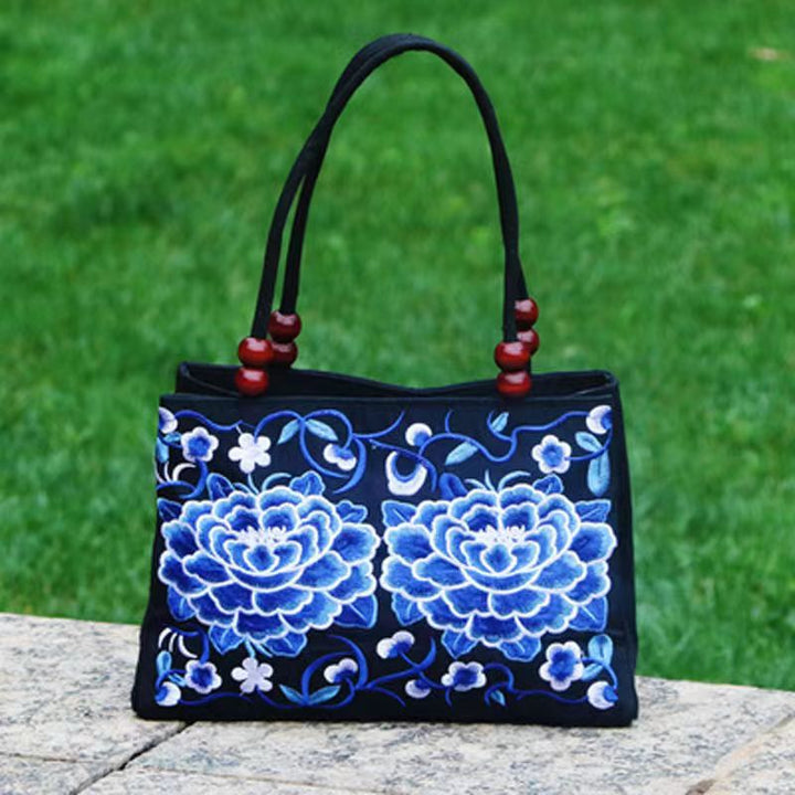 Black handbag with blue floral embroidery on a wooden surface with a green grass background