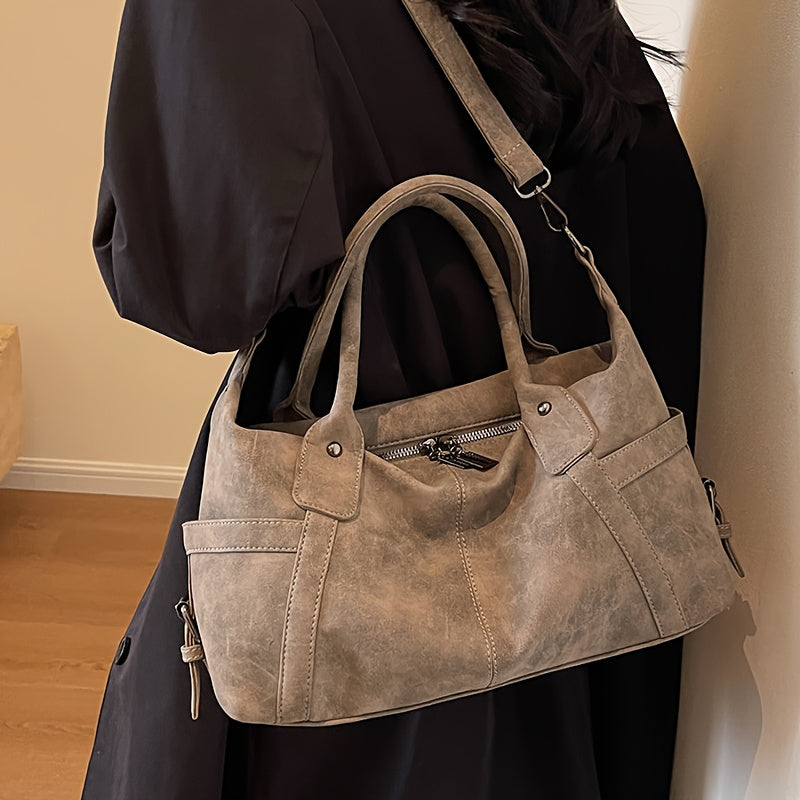 Brown suede handbag held by a person wearing a black outfit.