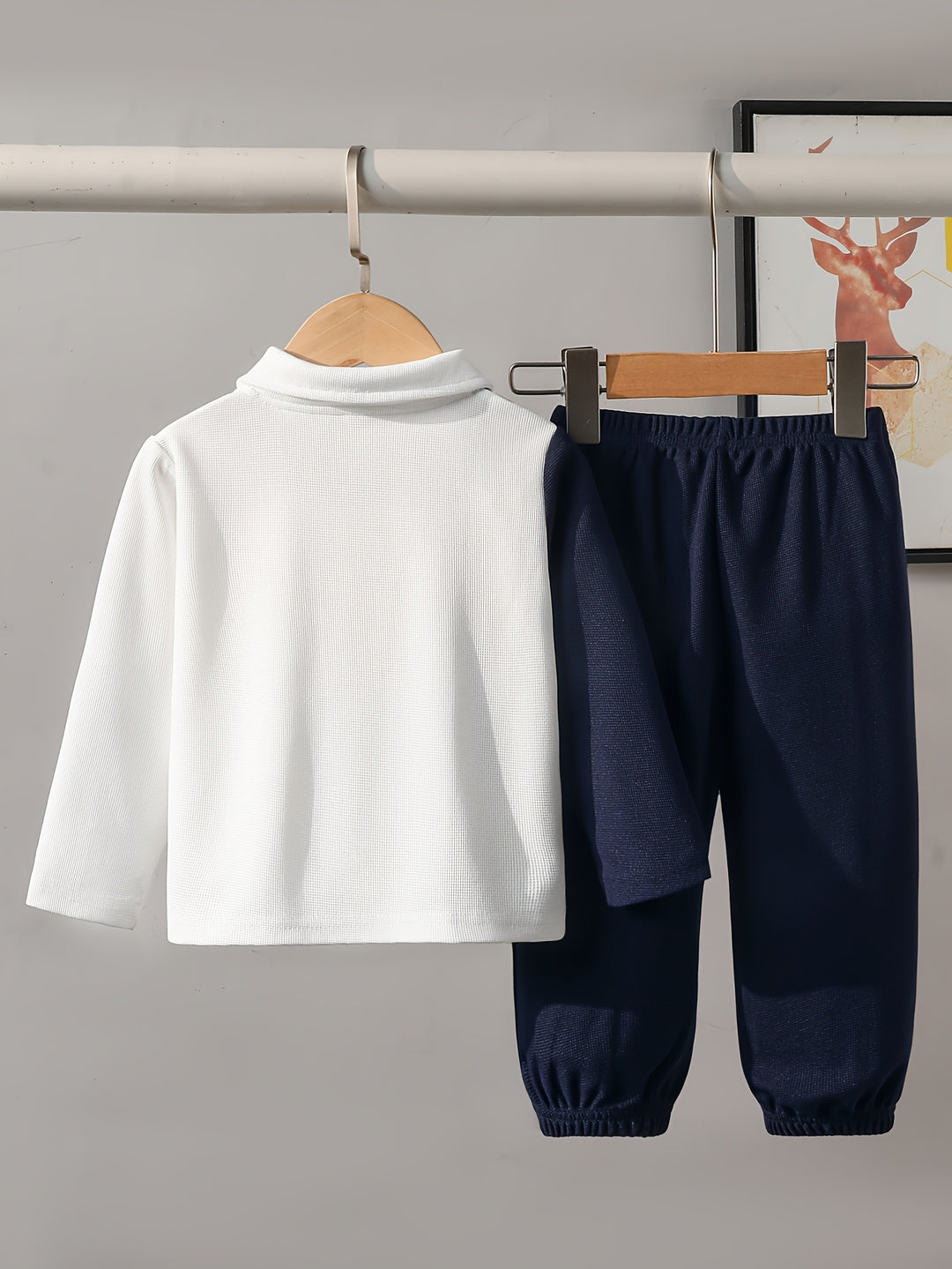 White long-sleeve shirt and navy pants hanging on a rack against a gray background.