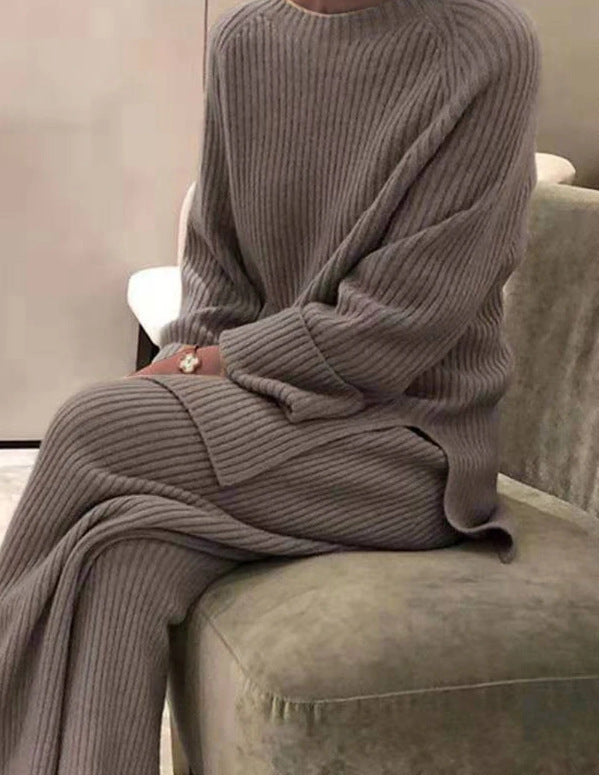 Person wearing a gray ribbed sweater and pants sitting on a couch.