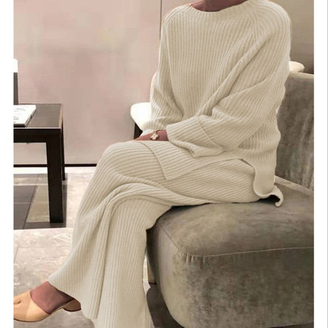 Person wearing a cream ribbed sweater and pants sitting on a gray sofa.