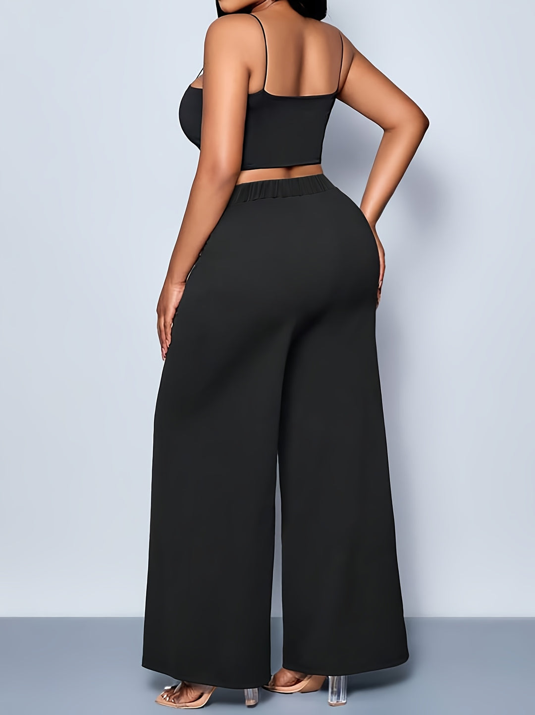 Person wearing a black outfit with wide-leg pants against a light gray background