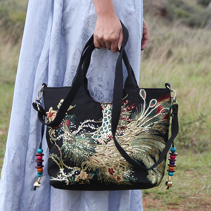 Person holding a black handbag with peacock design and colorful beads outdoors.
