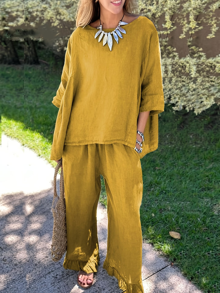 Woman wearing a mustard yellow outfit with a necklace, standing outdoors.