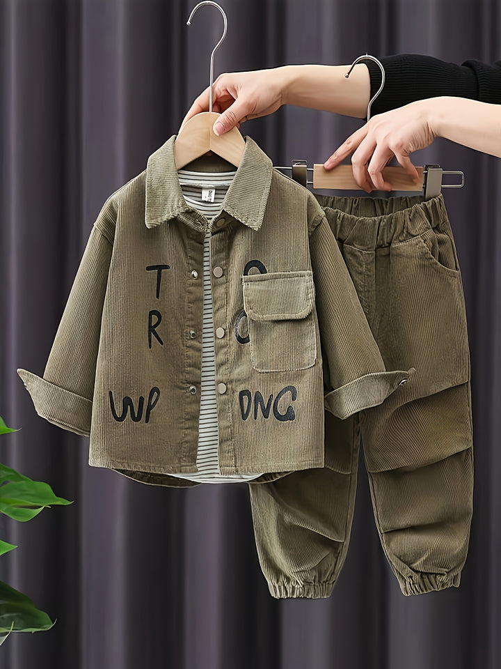 Children's green outfit with text on a hanger against a dark curtain background