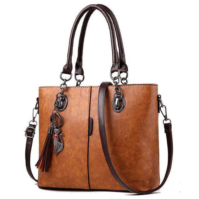 Large leather tote bag in tan with dual handles, shoulder strap, and tassel charm