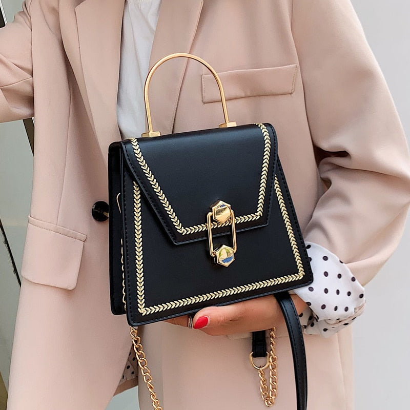 Black clutch handbag with gold metal handle, braided trim border, and front clasp lock