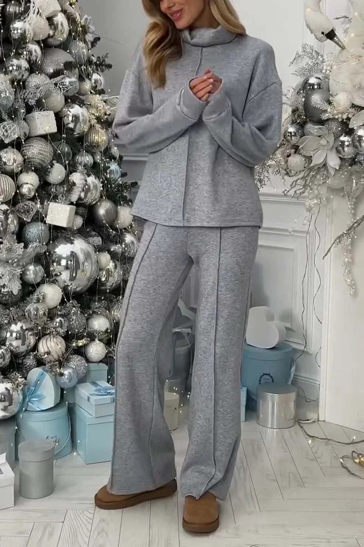 Woman in gray outfit standing in a room with decorative Christmas tree and presents.