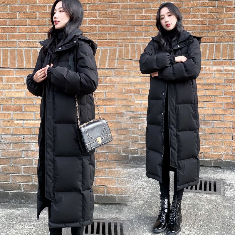 Women's Black Quilted Long Winter Coat Styled With A Shoulder Bag And Lace-Up Boots.