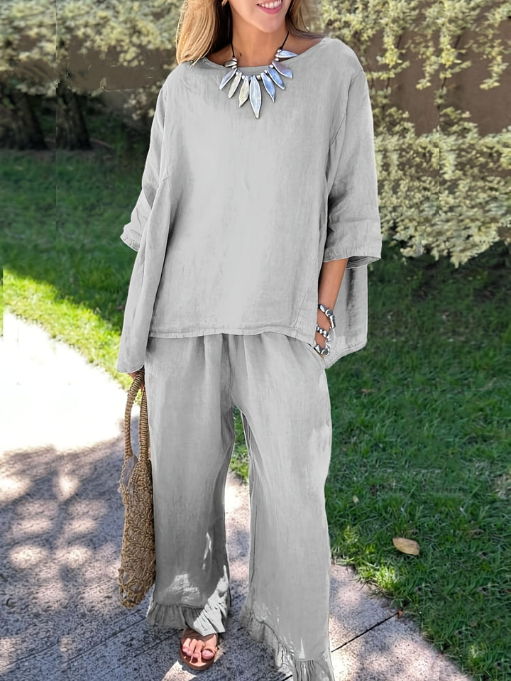 Woman wearing a gray outfit with wide-leg pants and a long-sleeve top, standing outdoors.