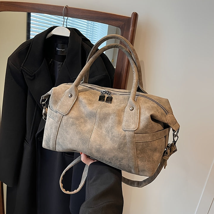 Brown leather handbag held in front of a black coat on a hanger.