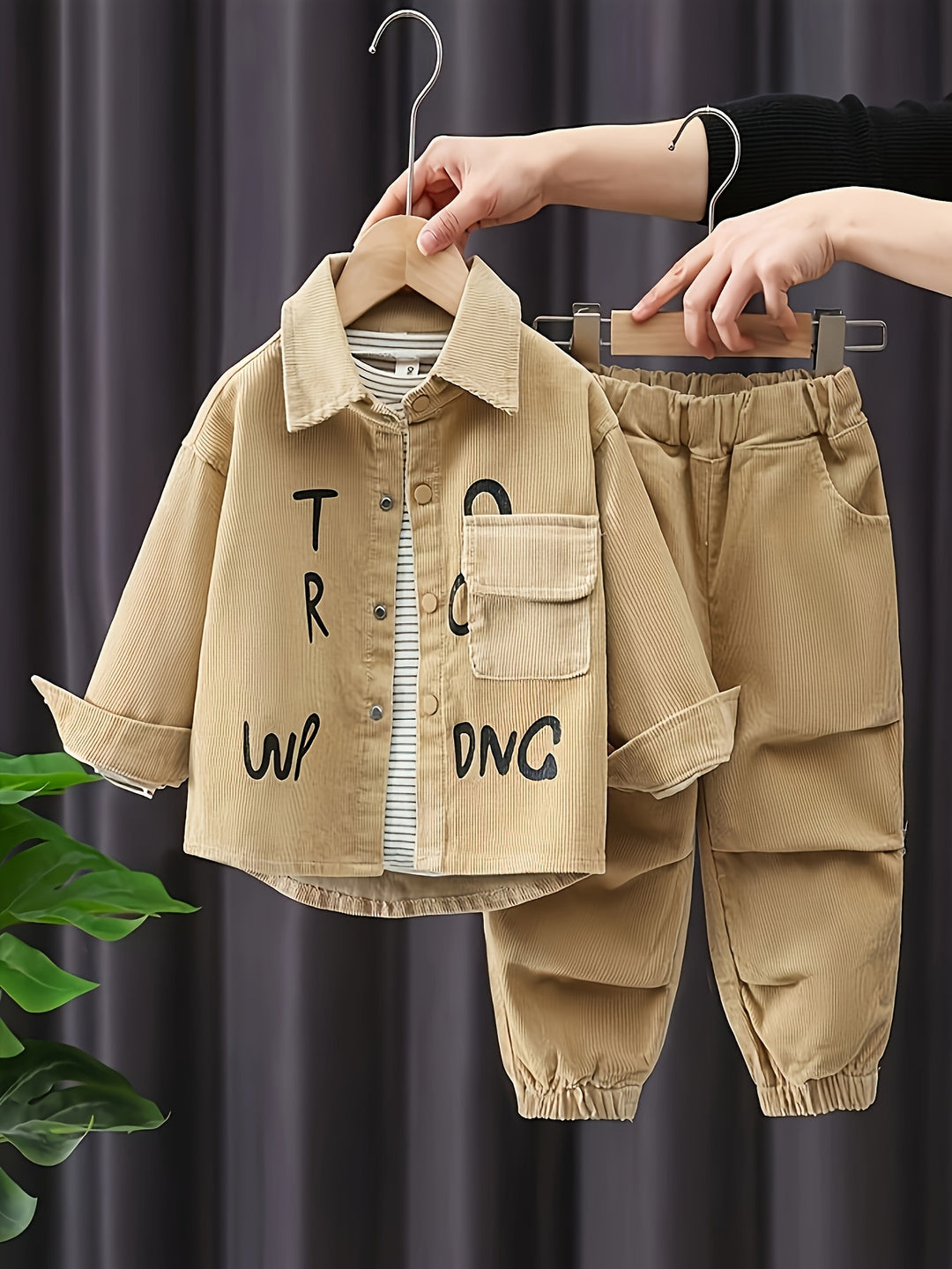 Children's beige outfit with text on a hanger against a dark background