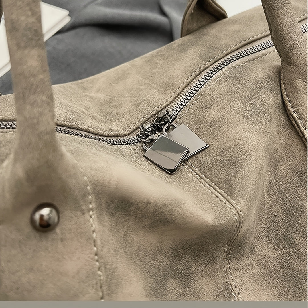 Close-up of a brown leather bag with a zipper and brand tag.