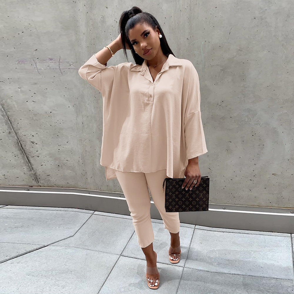 Woman in beige outfit holding a black clutch against a concrete wall.