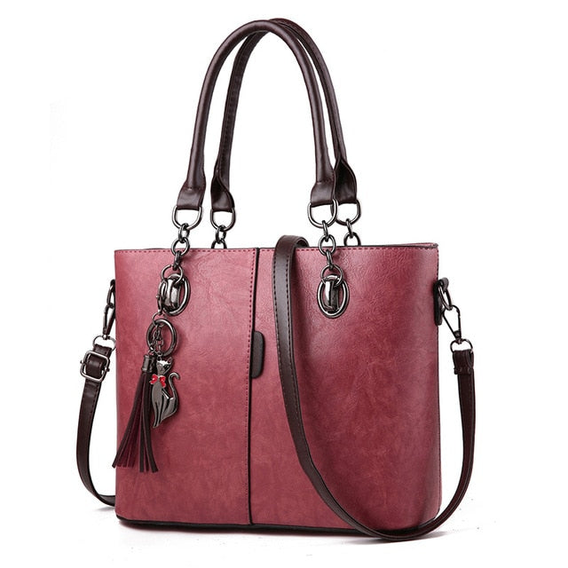 Plum leather tote bag with structured front, top handles, crossbody strap, tassel charm