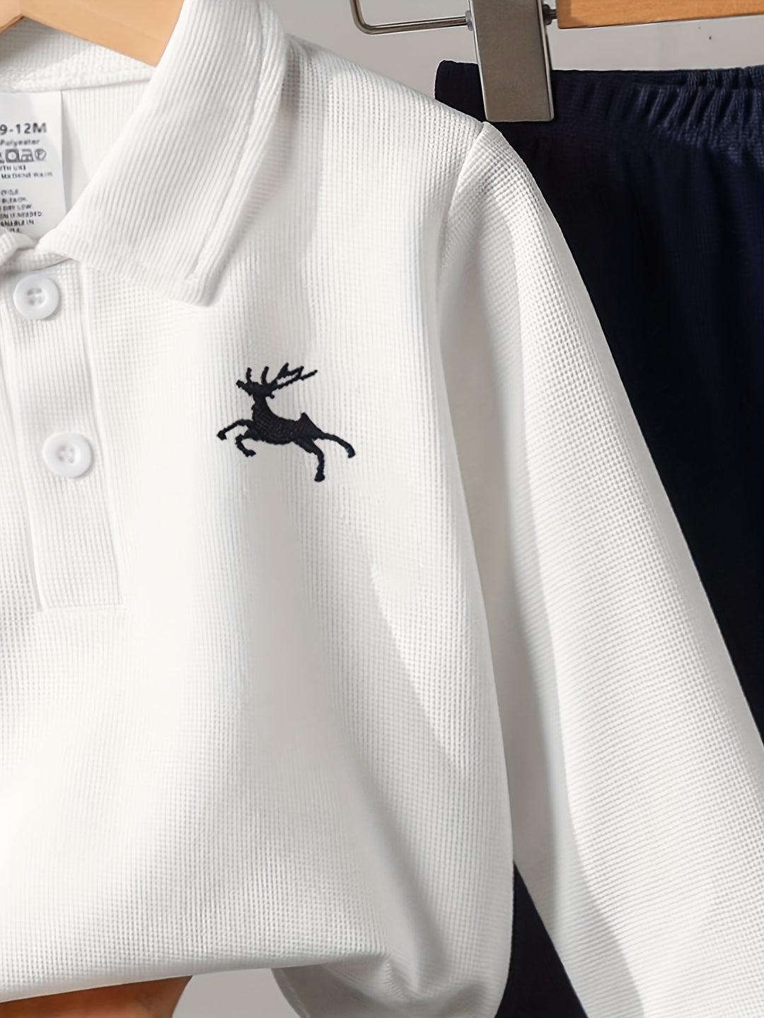 White polo shirt with a black deer logo on a hanger