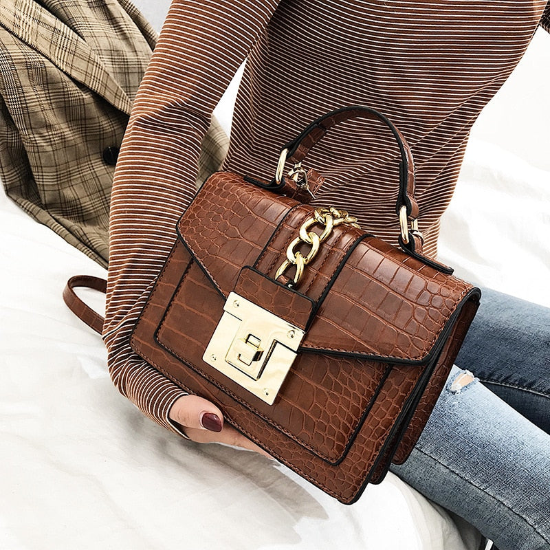 Brown crocodile-texture handbag with gold chain detail, front flap, and gold turn-lock clasp
