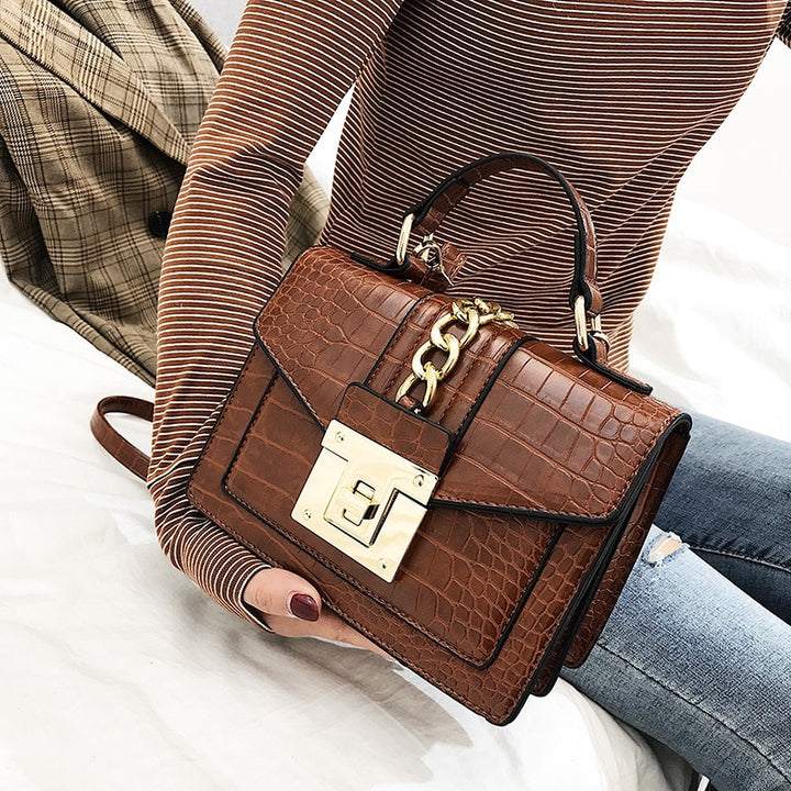 Brown crocodile-texture handbag with gold chain detail, front flap, and gold turn-lock clasp