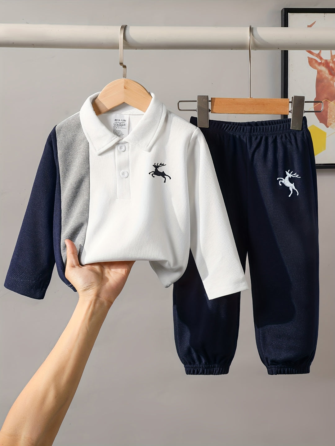 Children's polo shirt and pants set with a logo on a hanger against a gray background