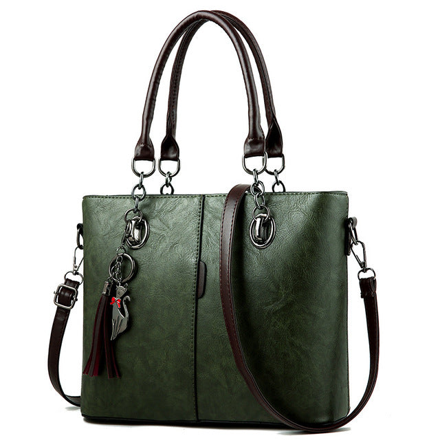 Green leather tote bag with structured front, top handles, crossbody strap, tassel charm