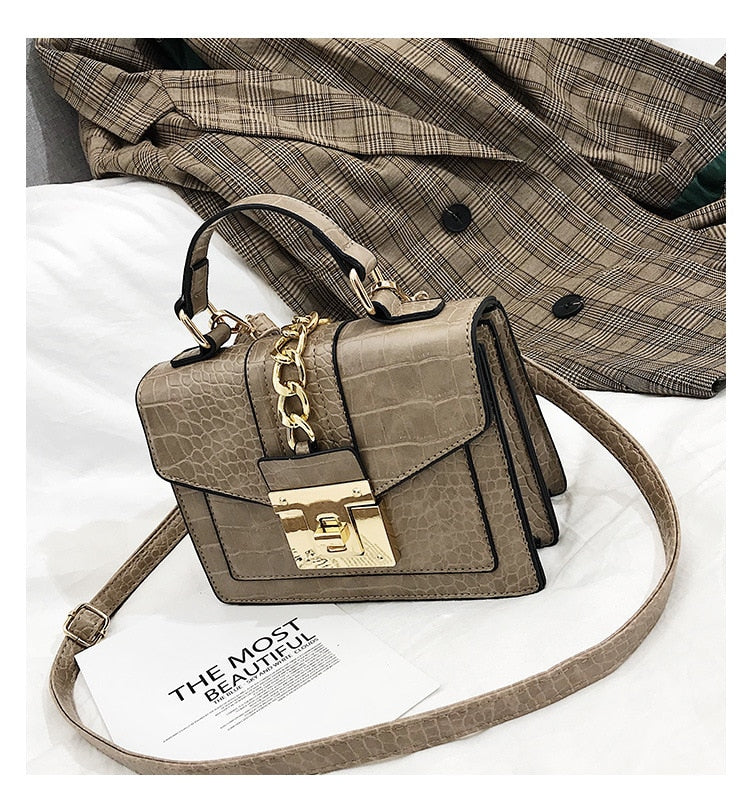 Light gray crocodile-texture handbag with chain strap, front flap, and gold turn-lock clasp