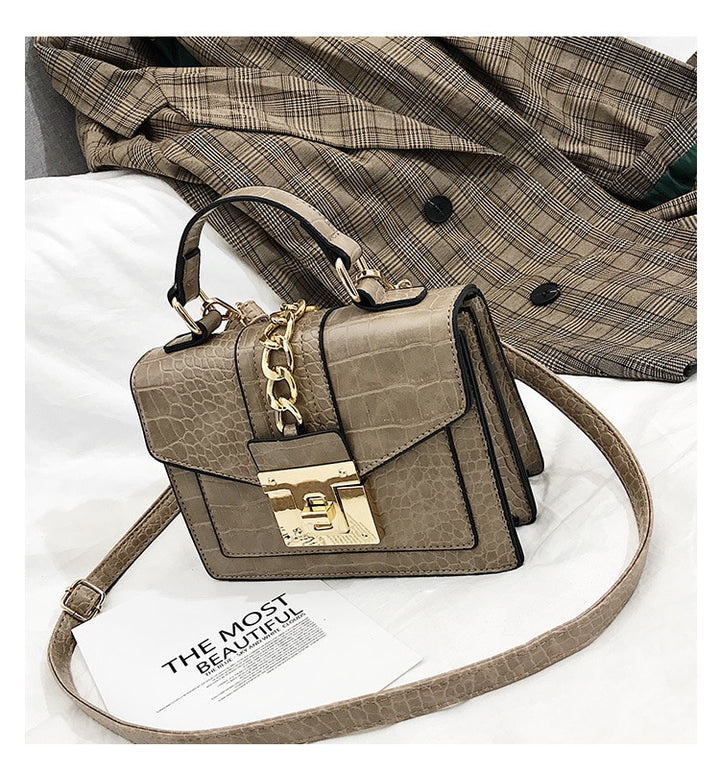 Light gray crocodile-texture handbag with chain strap, front flap, and gold turn-lock clasp