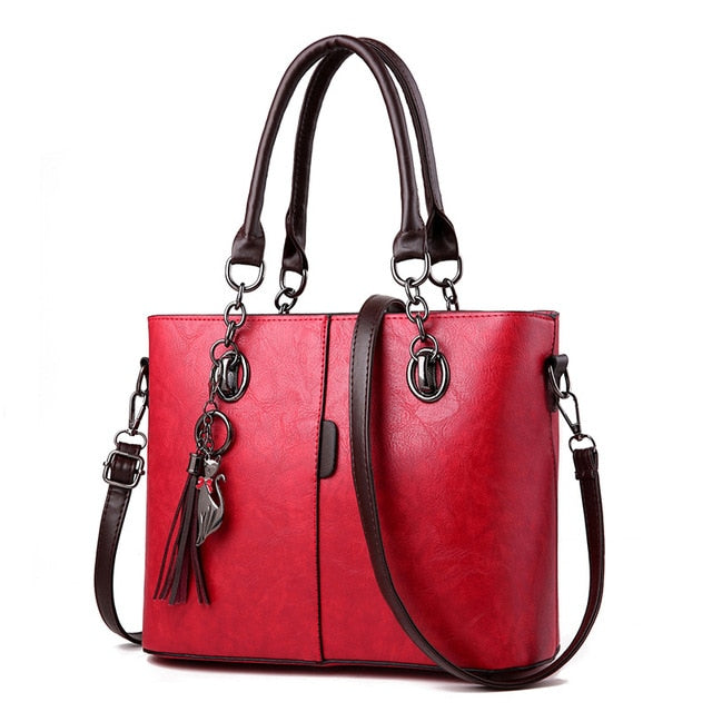 Large leather tote bag in red with dual handles, crossbody strap, and tassel keychain
