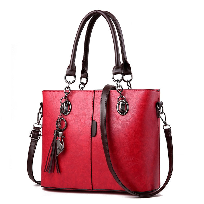 Red leather tote bag, structured, top handles, crossbody strap, tassel charm