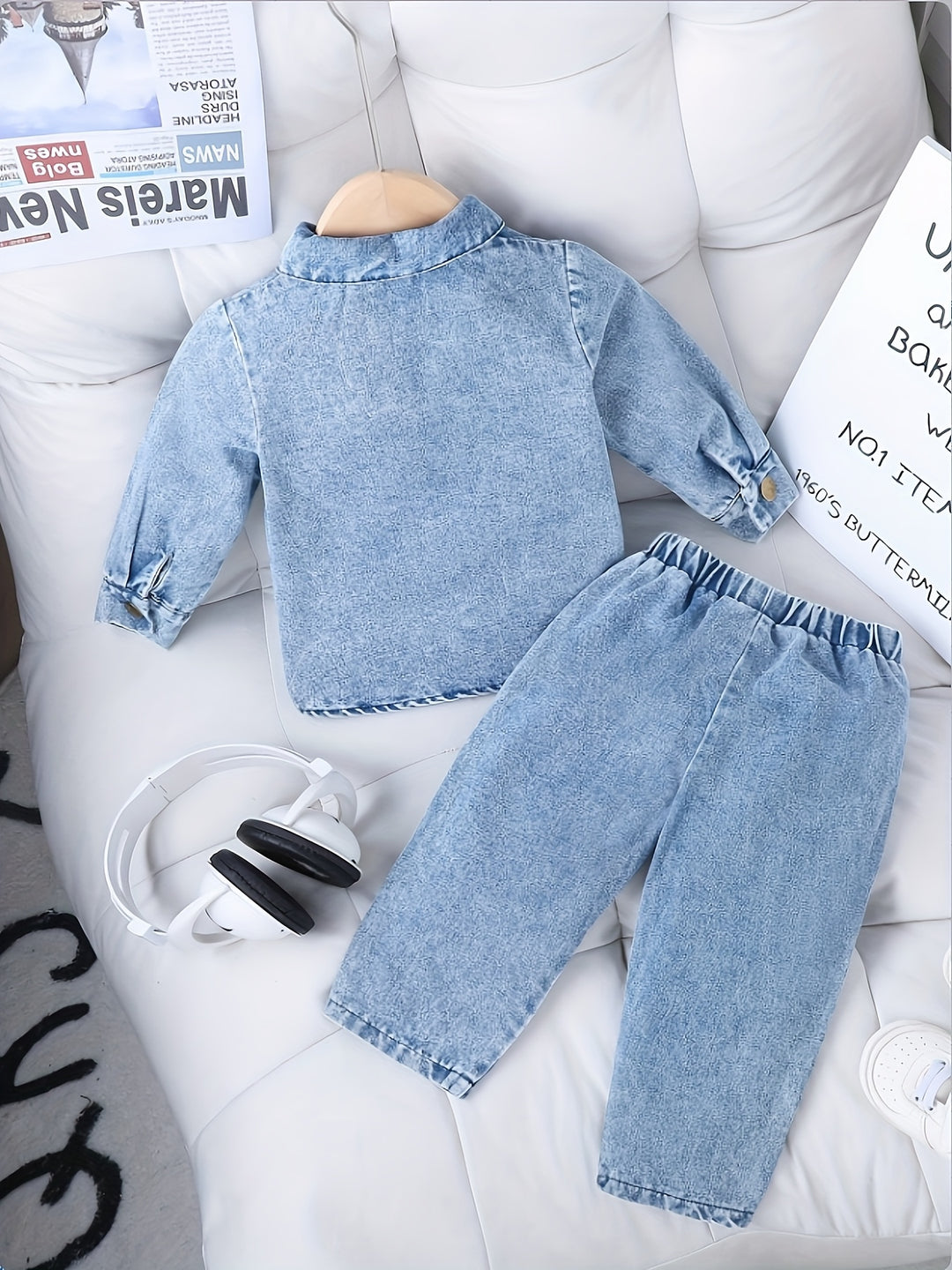 Children's denim outfit on a white surface with newspapers in the background