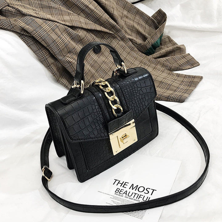Black crocodile-texture crossbody handbag with gold chain strap, front flap, and gold turn-lock clasp