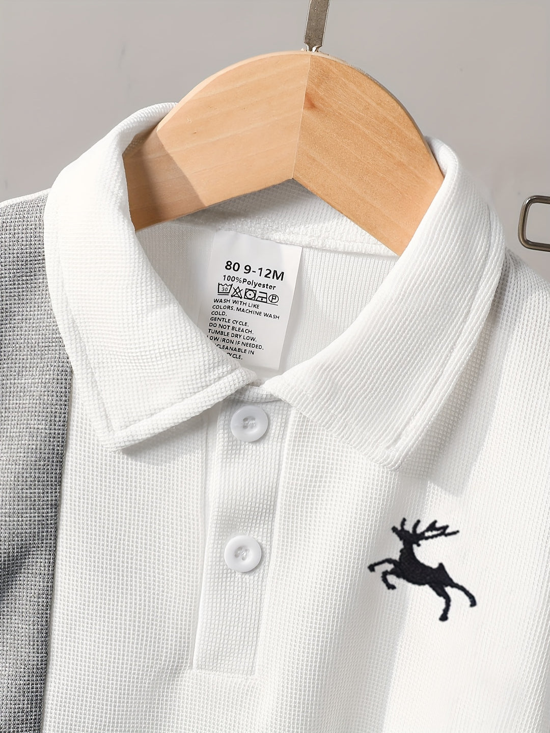White polo shirt with a black deer logo on a hanger against a gray background