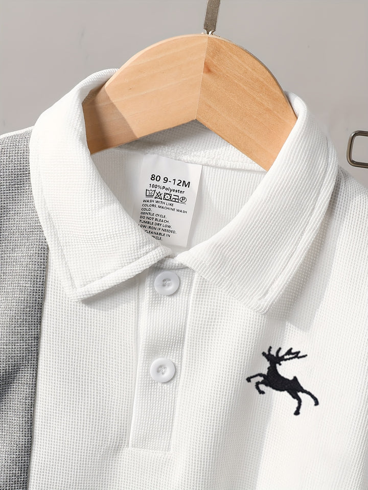 White polo shirt with a black deer logo on a hanger against a gray background