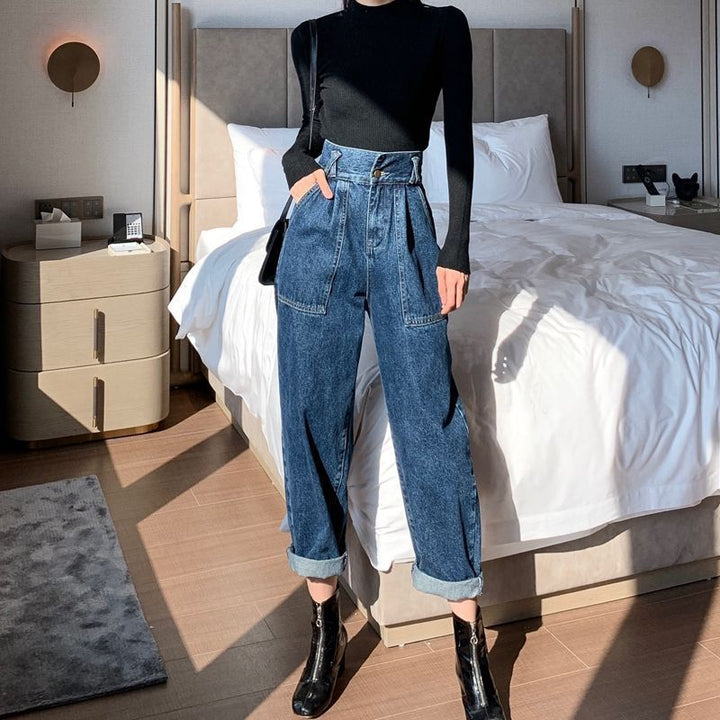 Person wearing a black top and blue jeans standing in a bedroom.