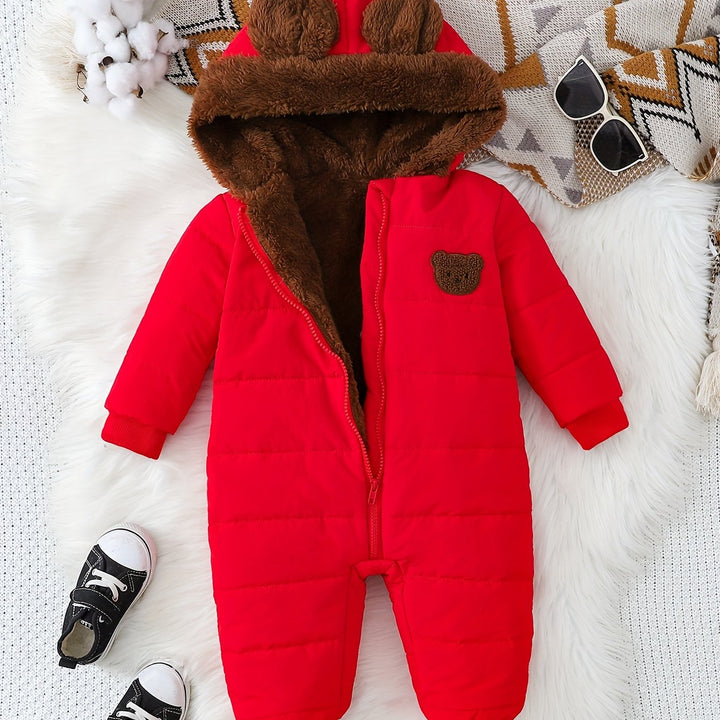 Red baby snowsuit with brown fur hood on a white surface, surrounded by accessories.