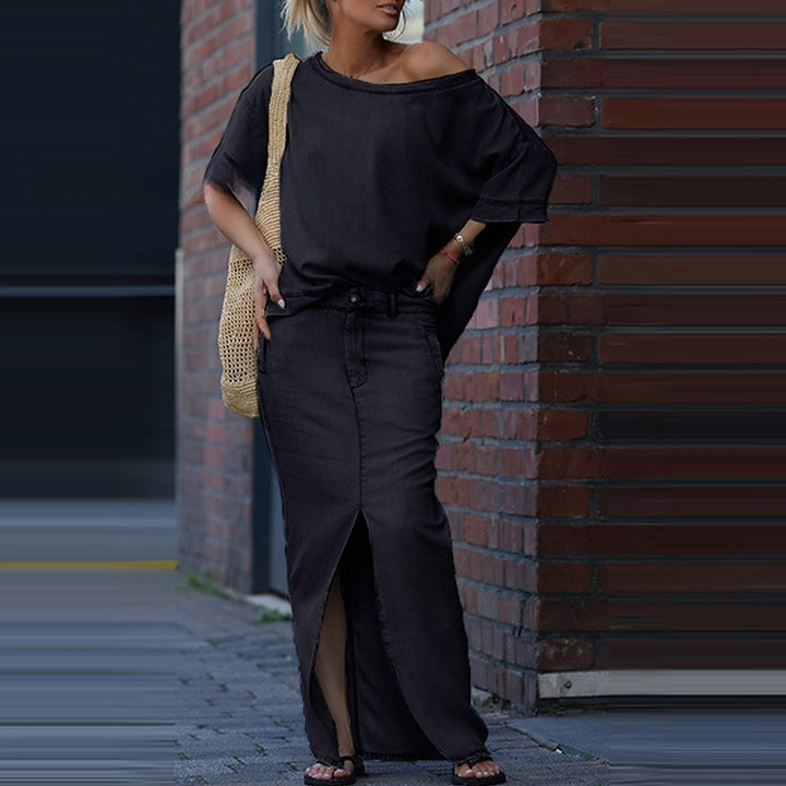 Woman wearing a black outfit with a textured bag against a brick wall.