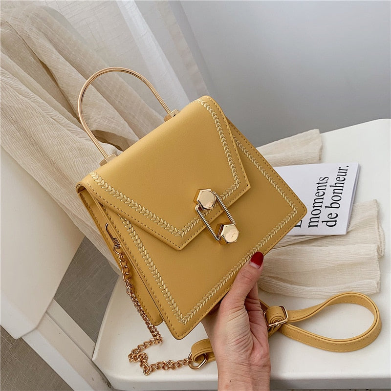 Beige clutch handbag with gold metal clasp, braided trim, and crossbody chain strap