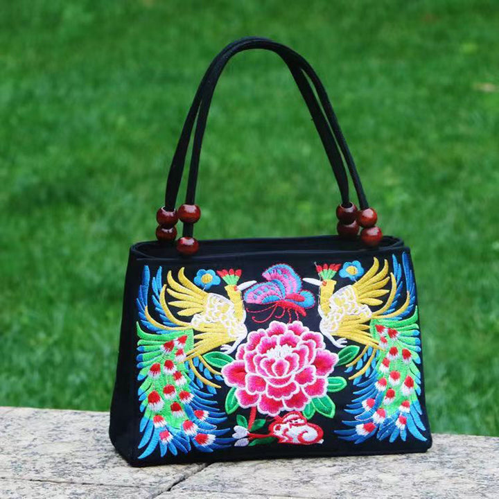 Black handbag with colorful floral and bird embroidery on a green grass background