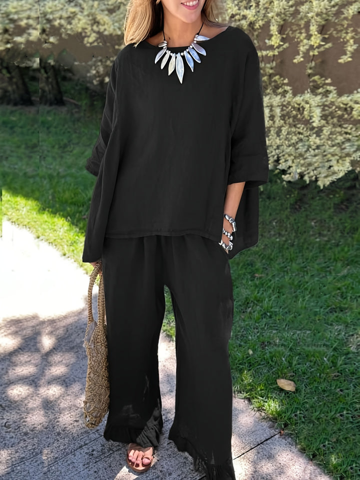 Woman wearing a black outfit with a necklace, standing outdoors on a sunny day.