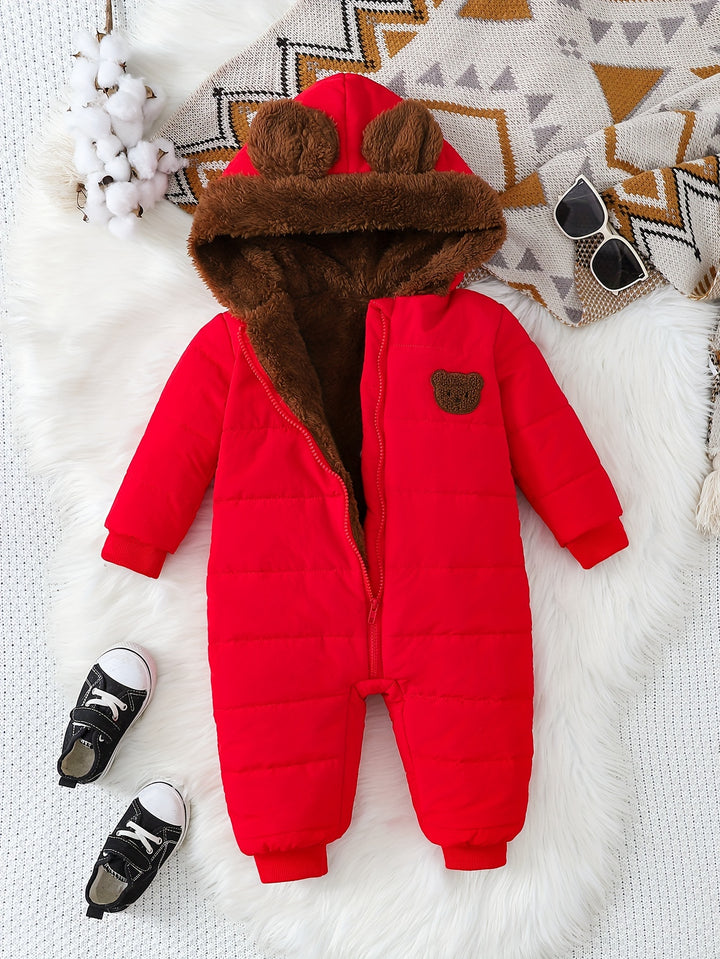 Red baby snowsuit with brown fur hood on a white surface with decorative items.