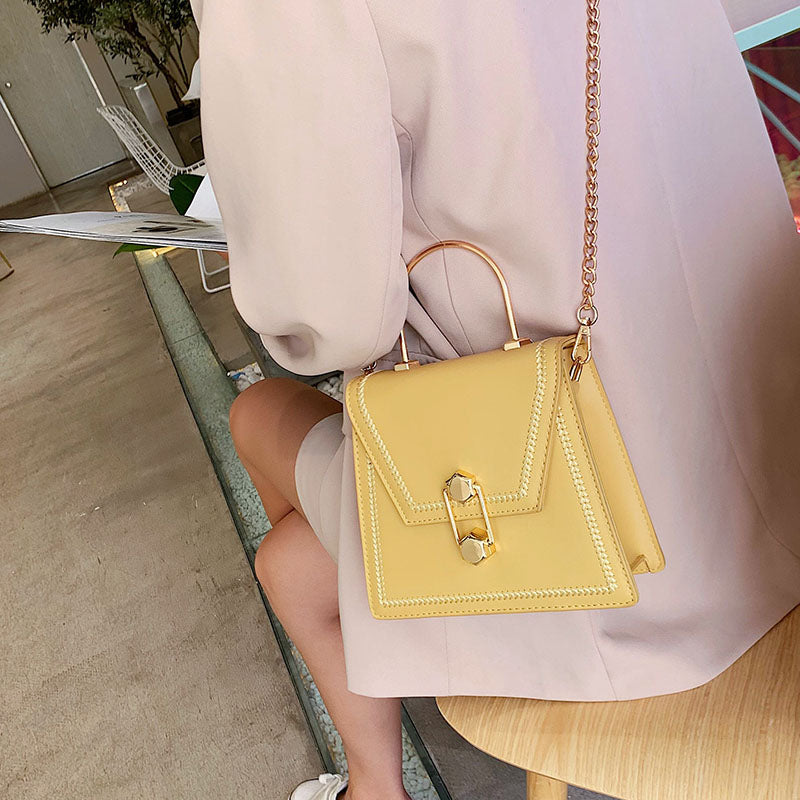 Yellow clutch handbag with gold metal handle, braided trim, and front clasp lock