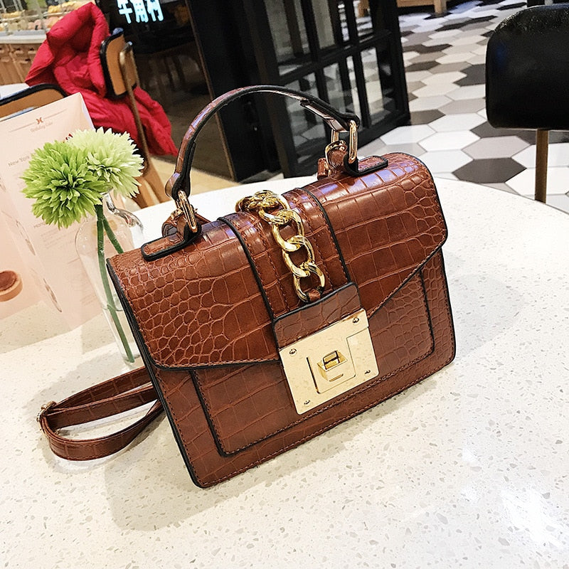 Brown crocodile-texture handbag with top handle, gold chain detail, and front flap turn-lock clasp