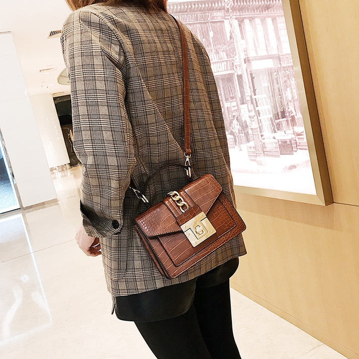 Brown crocodile-texture handbag with chain strap, front flap, and gold turn-lock clasp