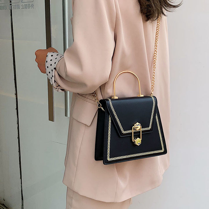 Black clutch handbag with gold metal handle, braided trim, and front clasp lock