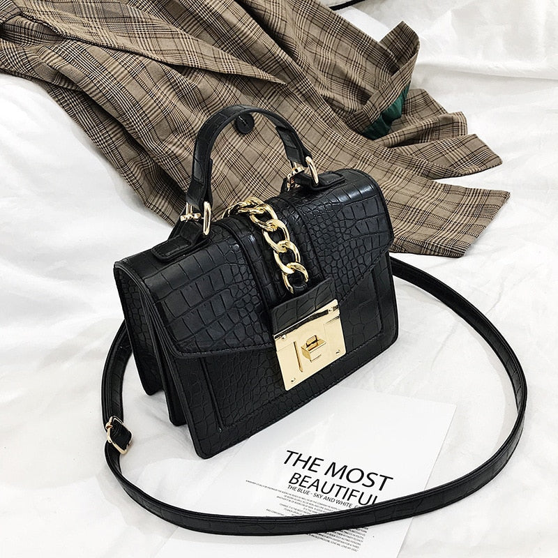 Black crocodile-texture handbag with gold chain strap, front flap, and gold turn-lock clasp