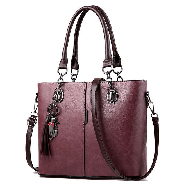 Large leather tote bag in plum with dual handles, shoulder strap, and tassel charm