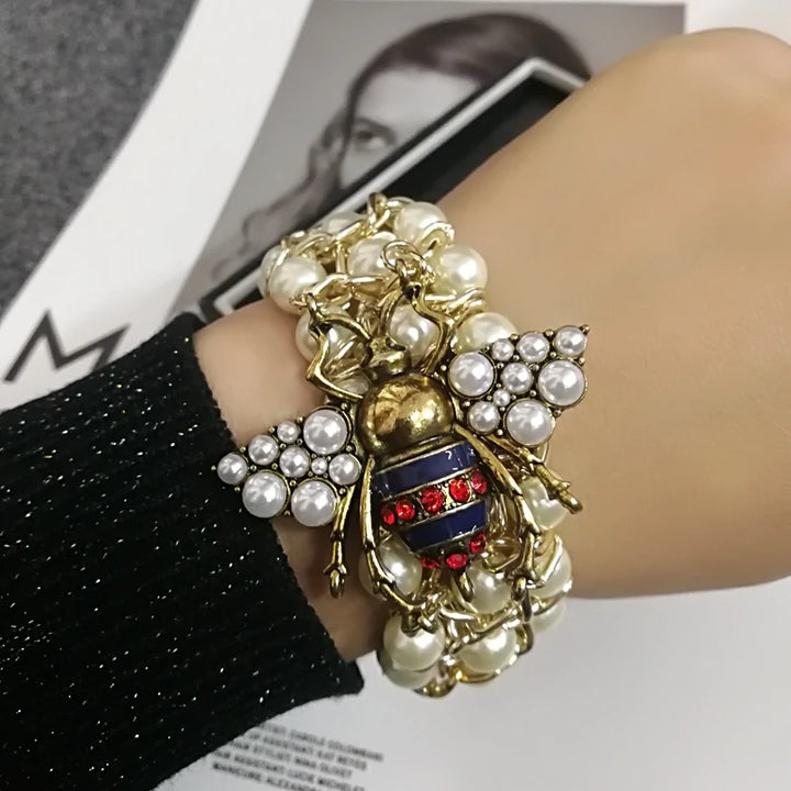 Bracelet with bee and pearl design worn on wrist, magazine in background