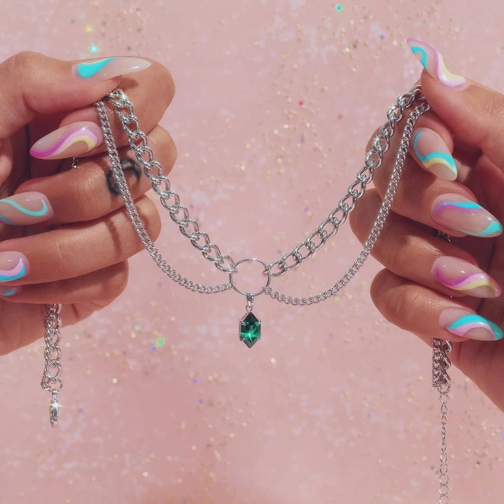 Layered chain necklace with green faceted teardrop pendant held in hands, silver-tone