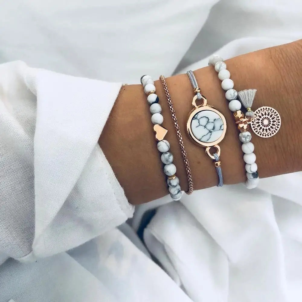 Set of charm bracelets on wrist: marble-look beads with tassel and gold-tone pendants