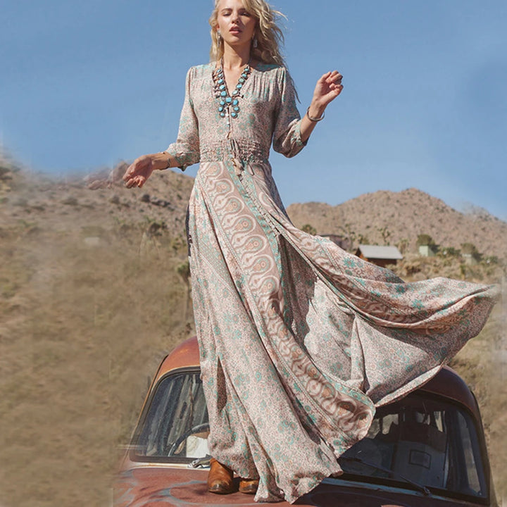 Woman in a long, patterned dress standing on an old car in a desert setting