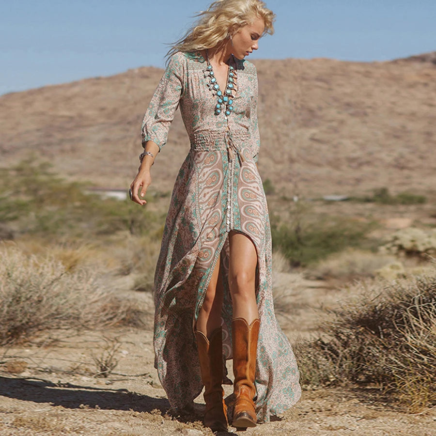 Woman in a long, patterned dress and boots walking in a desert landscape.